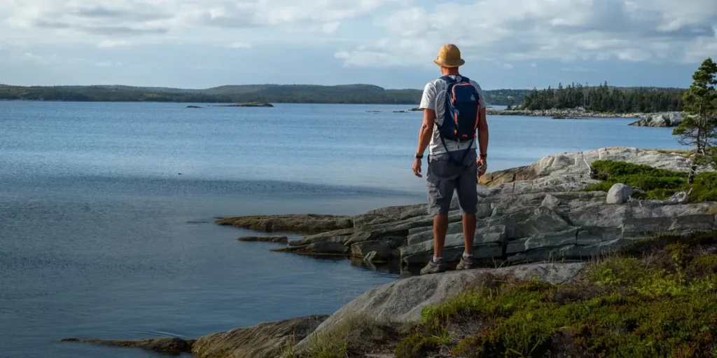 Hiker standing on granite rocks overlooking a coastal inlet on the Nova Scotia coastline